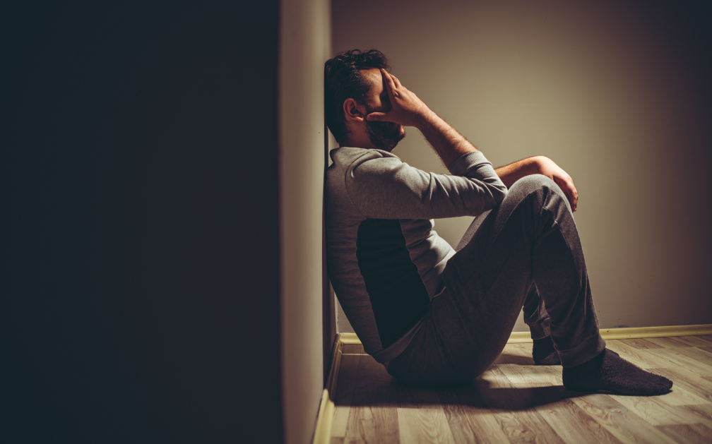 A man in despair is slumped against the wall to illustrate the concept of suicidal thoughts. The image accompanies an article about suicide and life insurance.