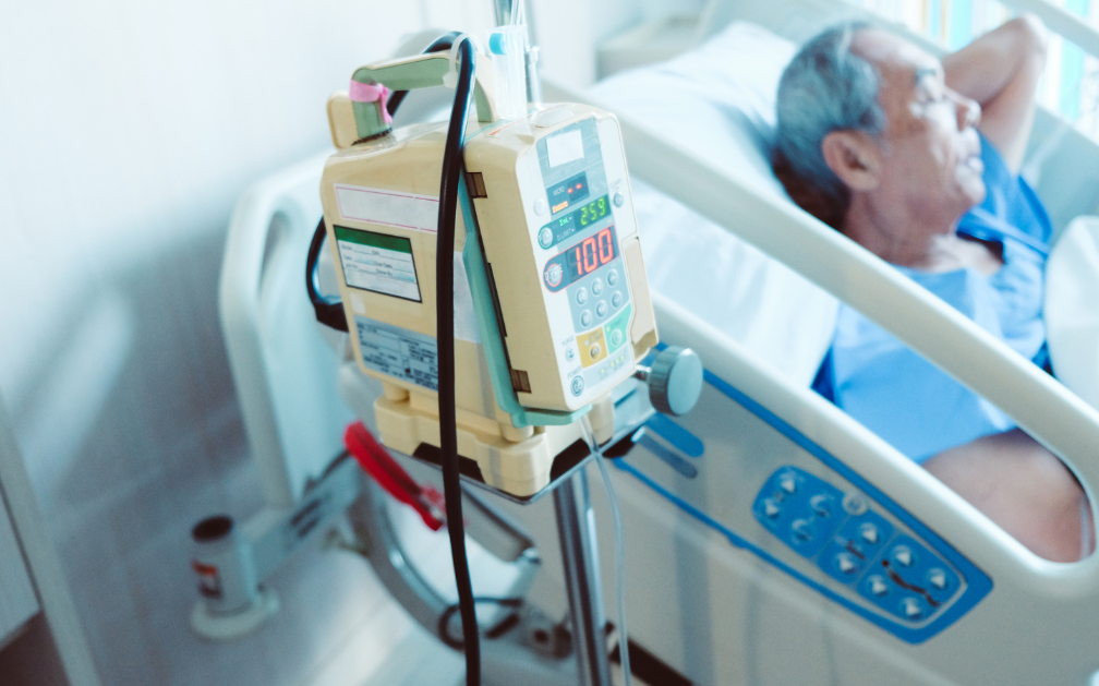 A man lies on a hospital bed. In the foreground is a machine measuring his vitals such as heartrate and blood oxygen levels. The image accompanies a blog post about term life insurance riders.