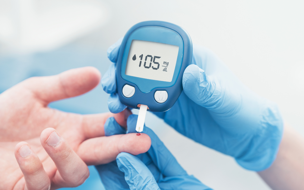 A gloved hand holds a glucose tester, which has pricked the finger of an ungloved hand. The tester reads 105. The image accompanies a blog post about getting life insurance if you’re a diabetic.